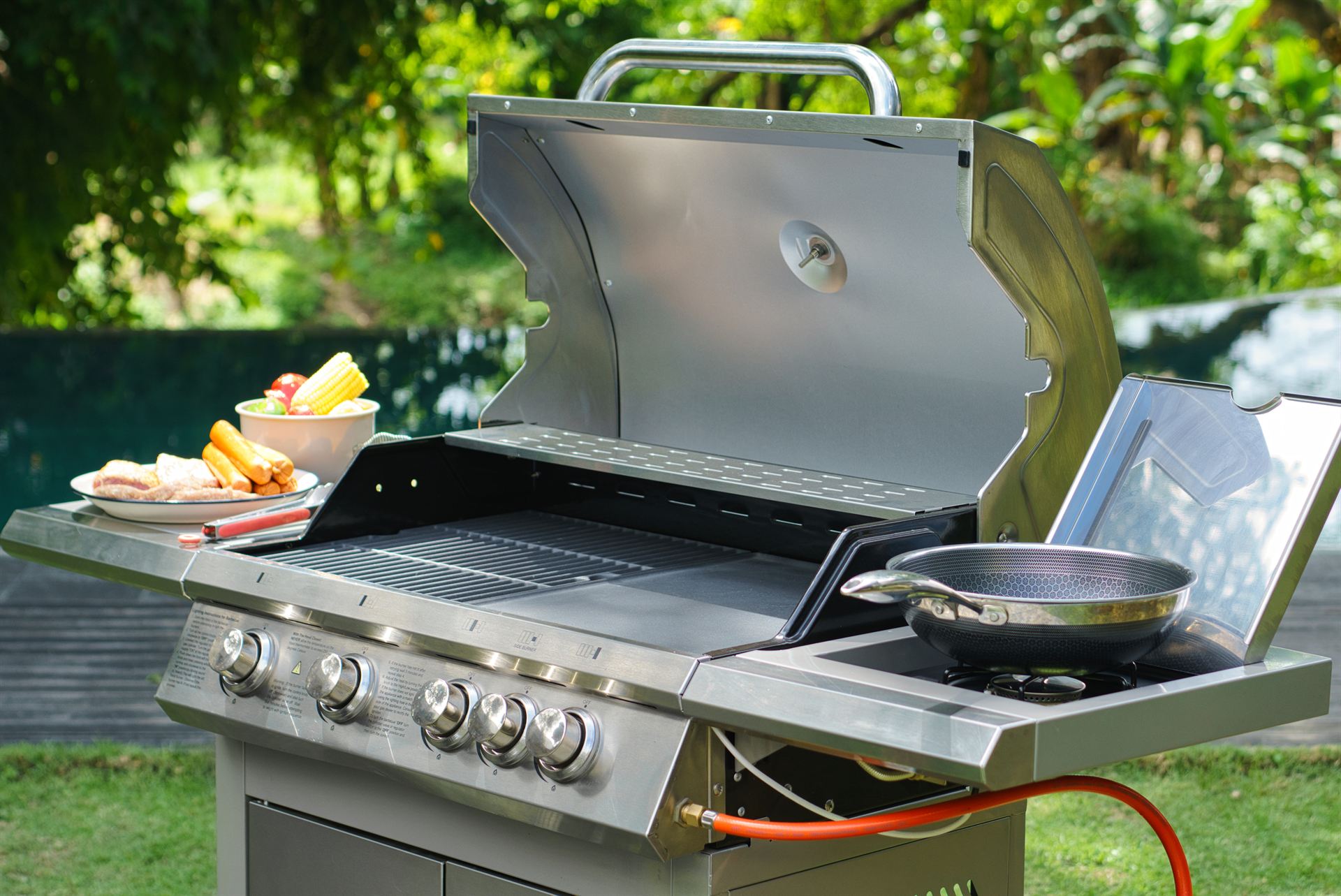 Full view of the stainless steel gas grill, hood open, beside a Bali villa pool